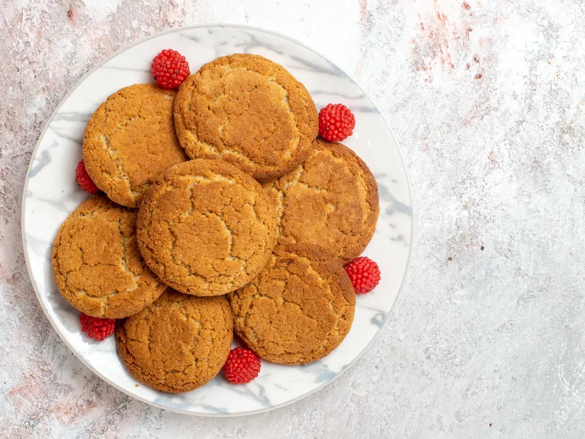 Galletas redondas y doradas en un plato de mármol, rodeadas de caramelos con forma de frambuesa.