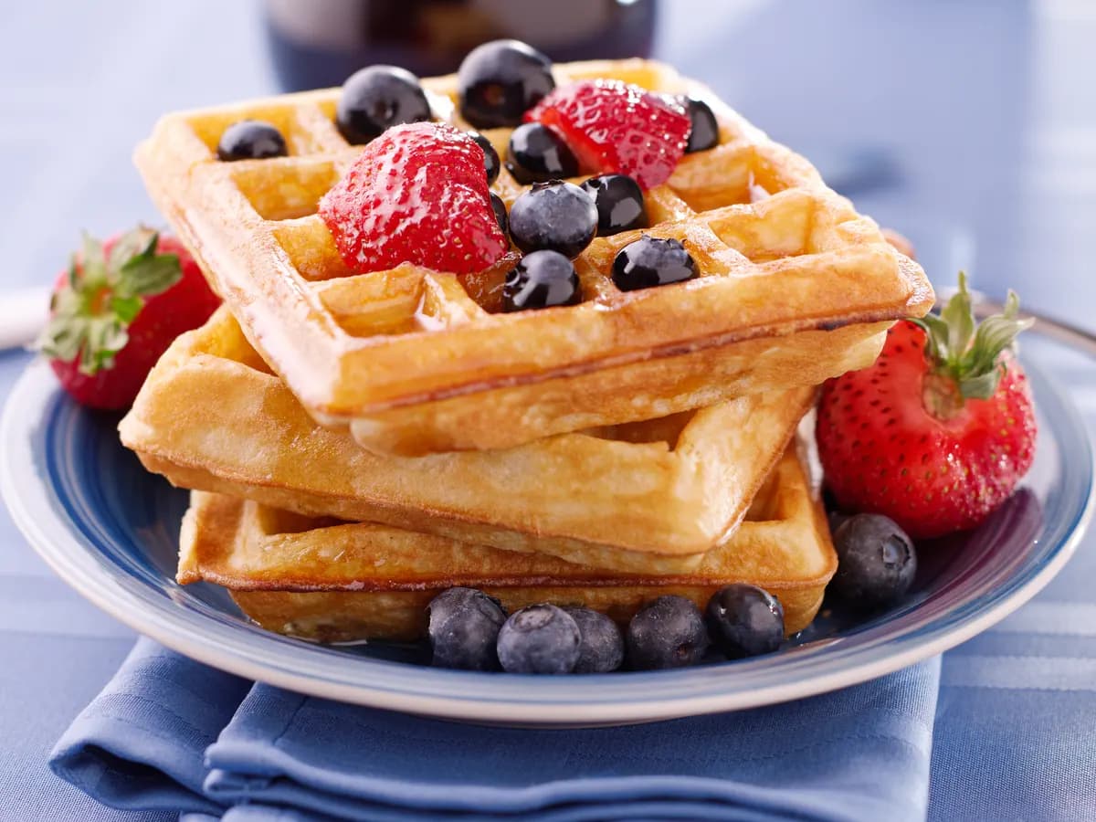 Tres gofres apilados en un plato azul, con fresas y arándanos por encima.