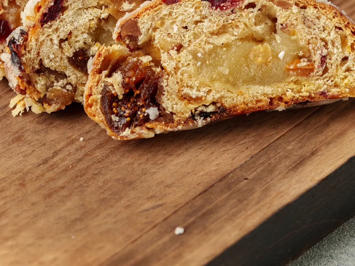 Rebanadas de un pan dulce con frutas confitadas y pasas, sobre una tabla de madera.